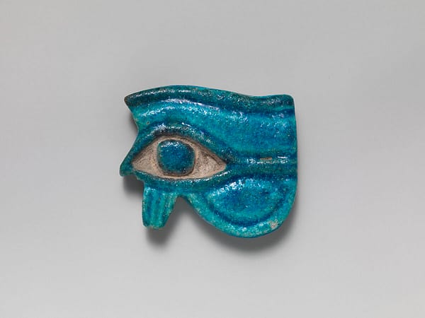 A bright and glowing faience wedjat, showing the left eye of horus, surrounded by faience stylised lines that form the eyebrow, eye, and lashes. The blue pupil is set in inset unglazed ceramic, making a striking contrast.
