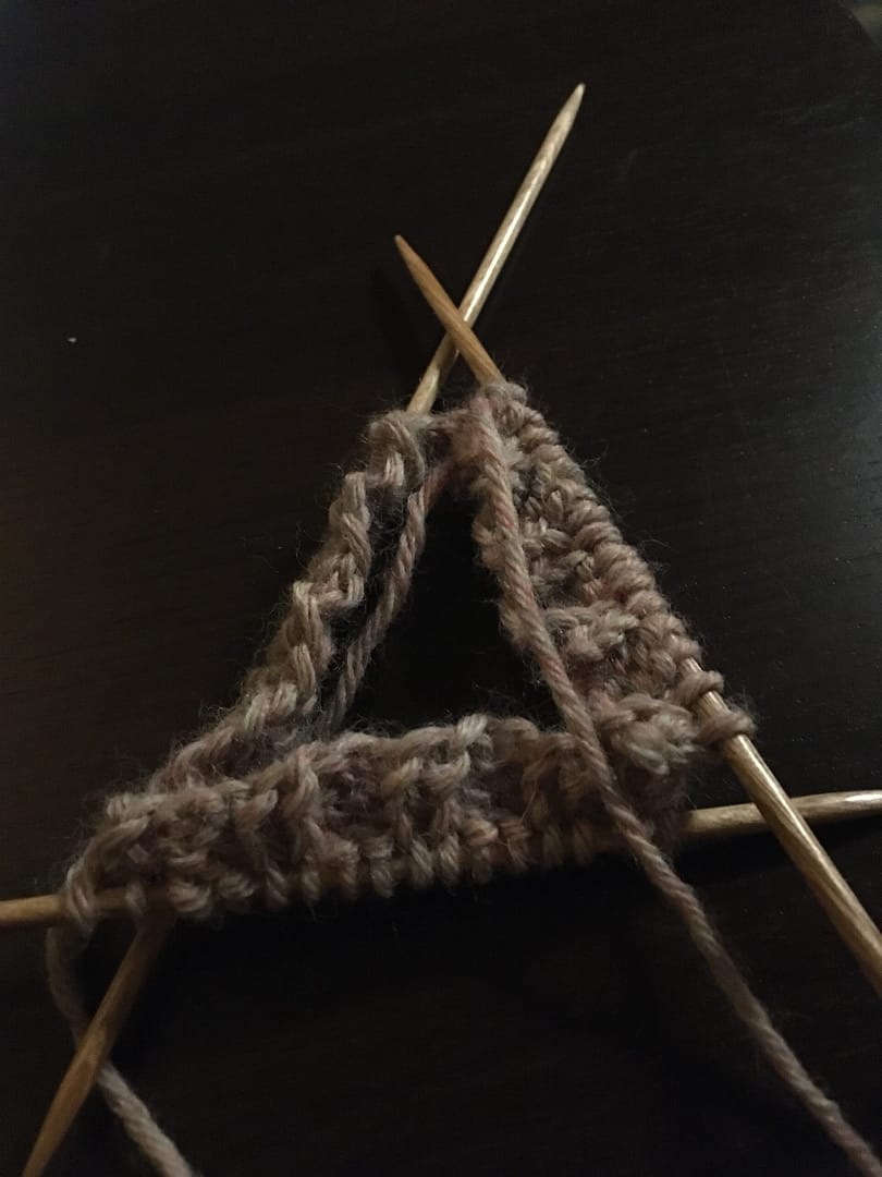 Three knitting needles with a few rows of stitches, laid in a triangular pattern.